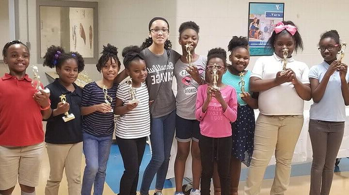 Madison is taking a photo with a group of students holding trophies